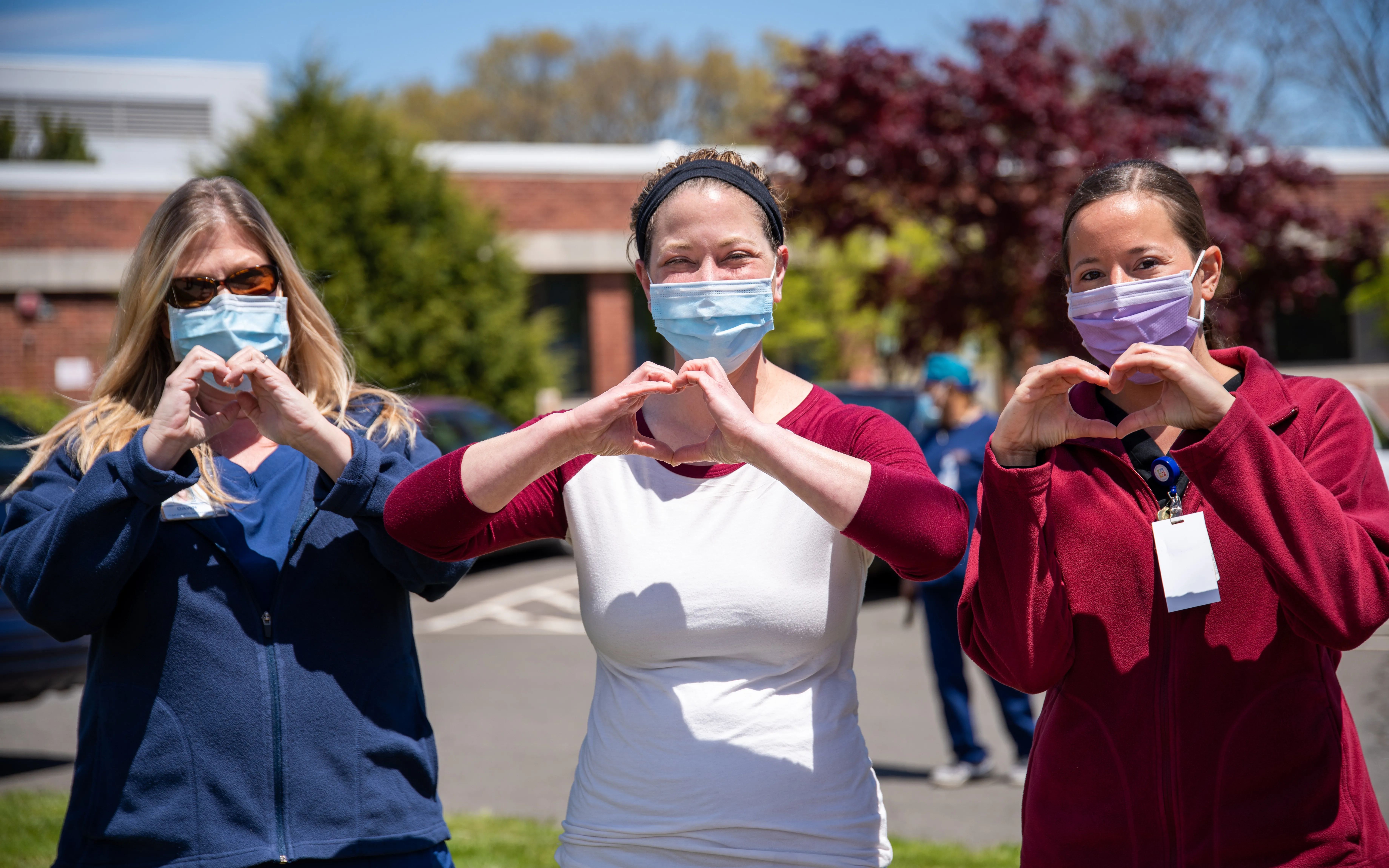 Three female nurses holding up heart hands outside