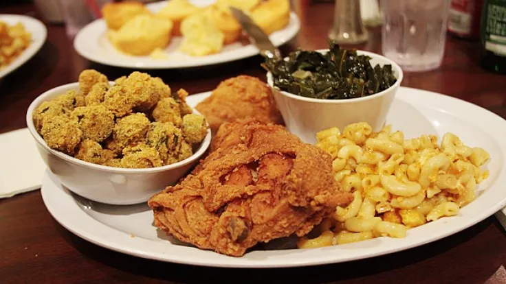 A plate of fried chicken, fried oysters, mac and cheese, and collard greens on a table